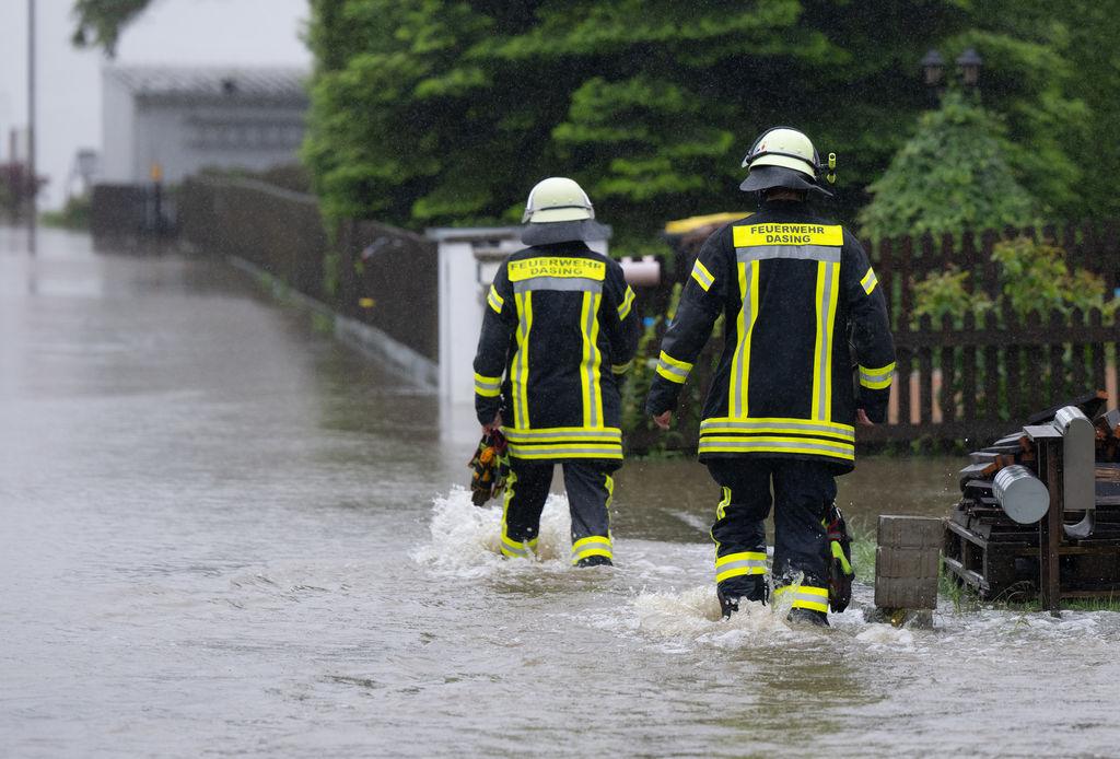 Bayern, Dasing: Feuerwehrleute gehen über eine überflutet Straße in Dasing.