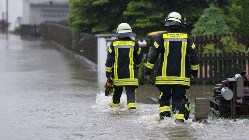 Bayern, Dasing: Feuerwehrleute gehen über eine überflutet Straße in Dasing.