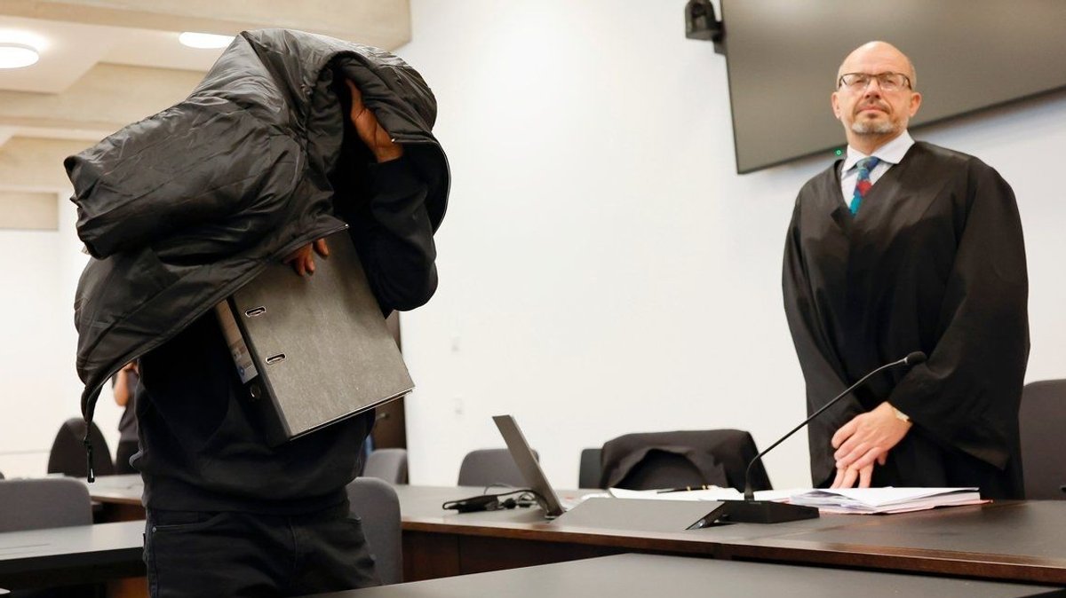 Der Angeklagte (links) versteckt im Gerichtssaal sei Gesicht unter einer Jacke. 