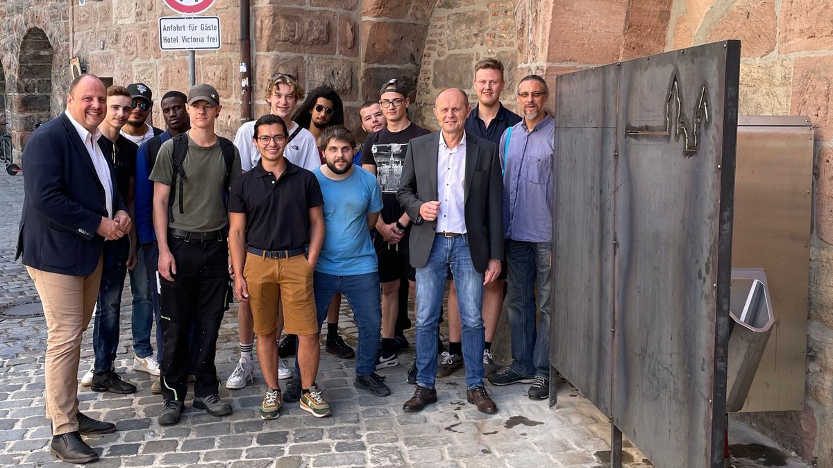 Eine Gruppe Männer steht an der Nürnberger Stadtmauer neben einem Edelstahl-Urinal.