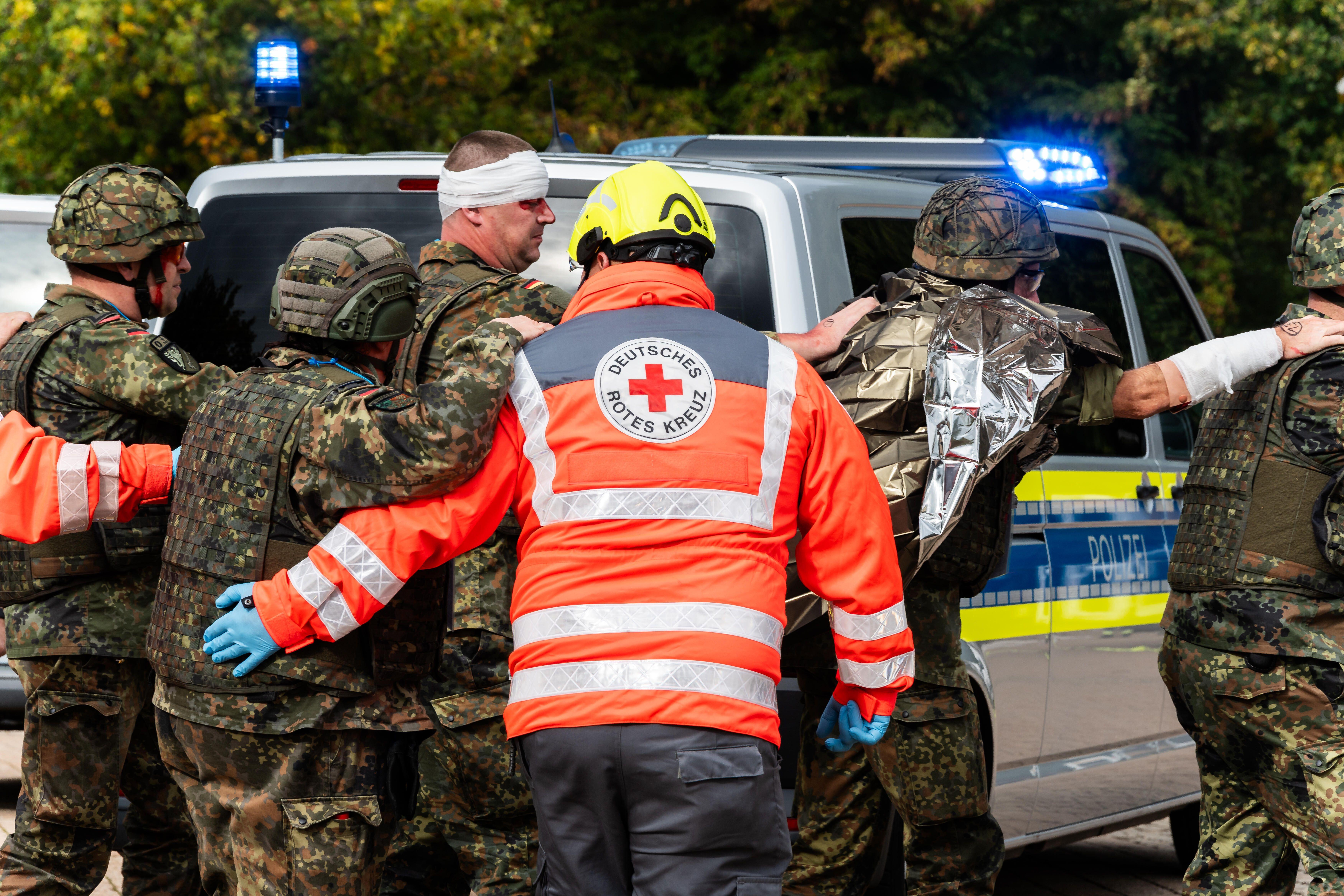 Auf dem Bild sind Sanitäter und Soldaten zu sehen, die eine verletzte Person abtransportieren. 