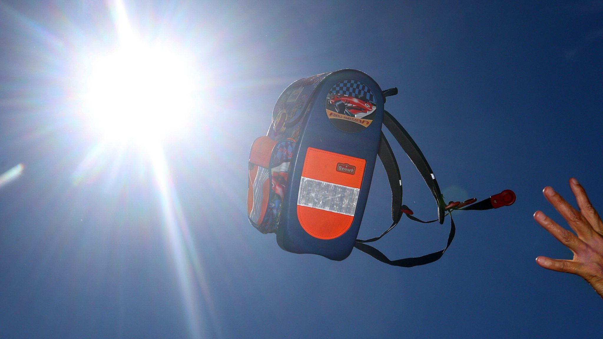 Ein Schulranzen wird vor dem sonnigen Himmel hochgeworfen.