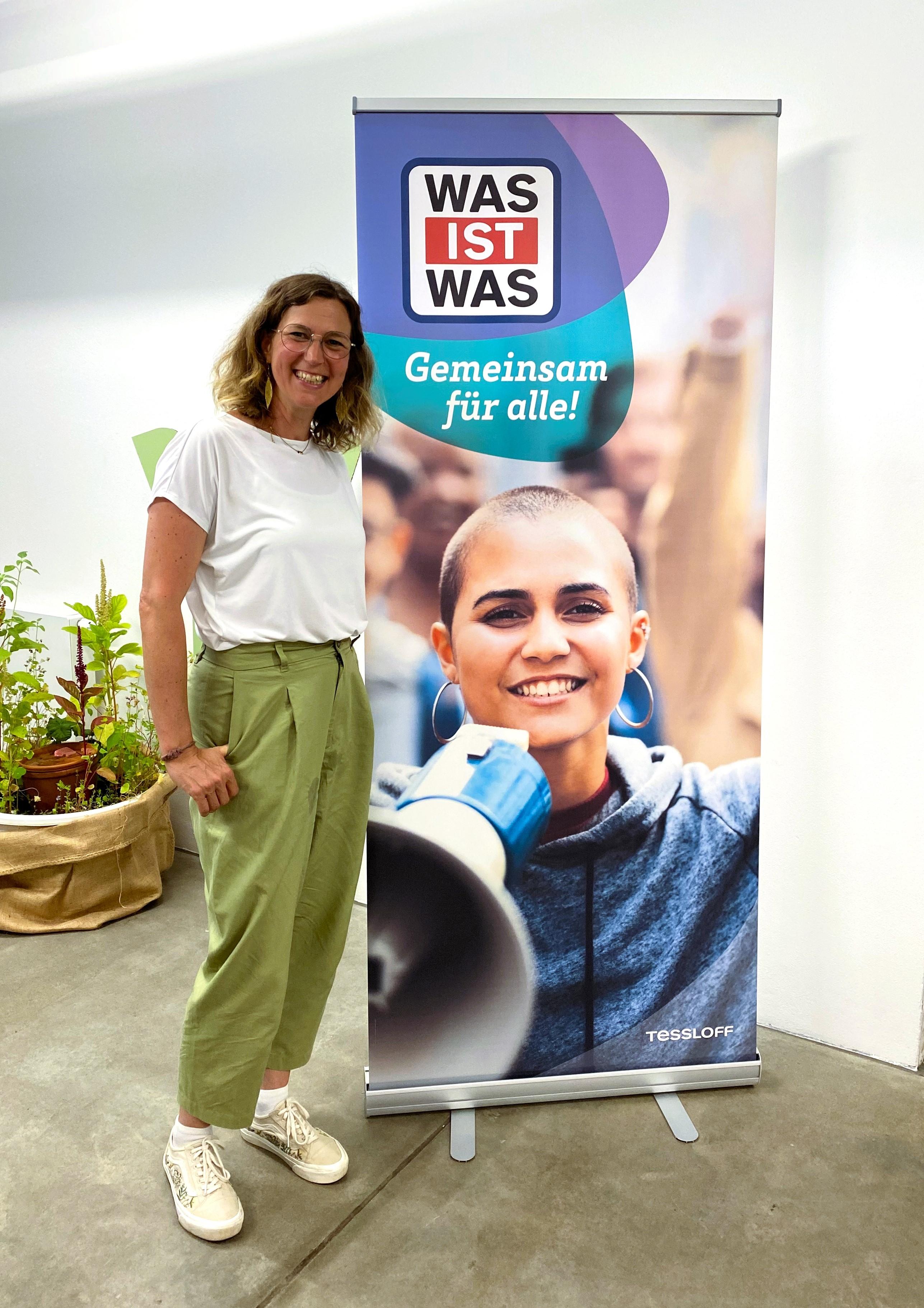 Autorin Andrea Weller-Essers steht vor einem Plakat für ihr neues Buch.