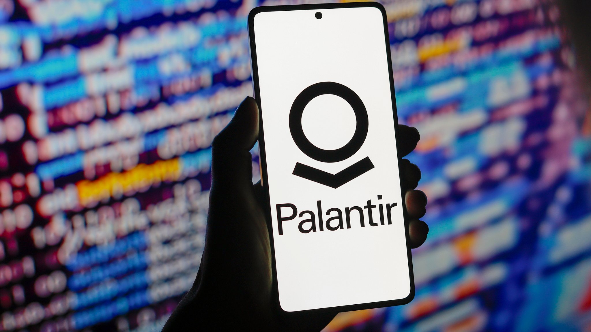 Hand halt ein Smartphone auf dem das Palantir-Logo sowie der Schriftzug zu sehen sind (Symbolbild)