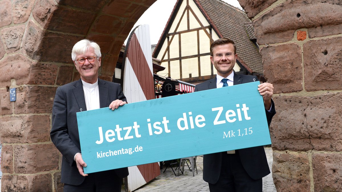 Zwei Männer halten ein Schild mit der Aufschrift "Jetzt ist die Zeit", kirchentag.de.