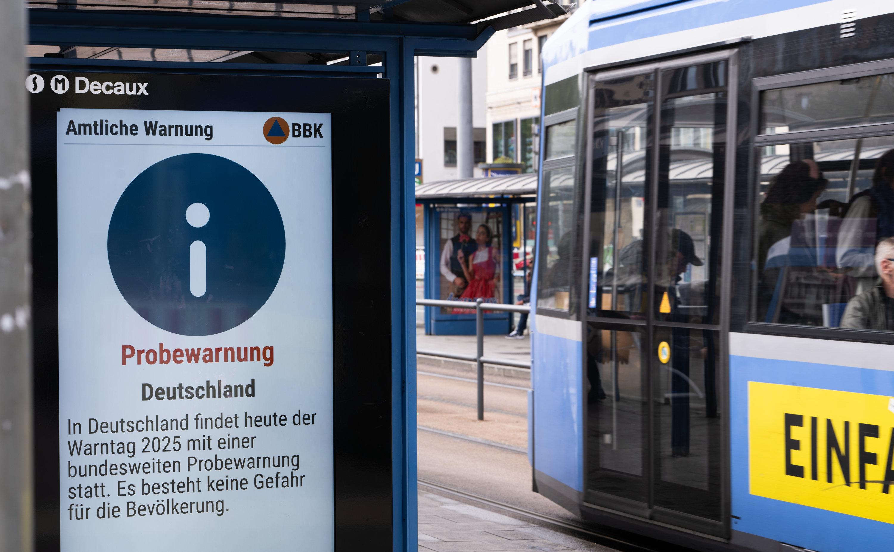 An einer Tramhaltestelle am Stachus in München ist eine Meldung zum Probealarm auf einer Anzeigetafel zu sehen.