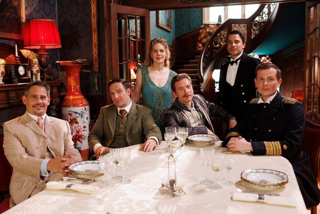 Mister Pommeroy (Moritz Bleibtreu), Mister Winterbottom (Frederick Lau), Sir Toby (Jacob Matschenz) und Admiral von Schneider (Christoph Schechinger, v.l.n.r.) - dahinter die junge Miss Sophie (Alicia von Rittberg) und Butler James (Kostja Ullmann), undatierte Szene aus "Start des "Dinner for One"-Prequels "Miss Sophie - Same Procedure as Every Year" auf Amazon Prime Video. 