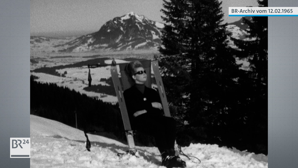 Frau im aus Skiern gebauten Liegestuhl vor Bergpanorama