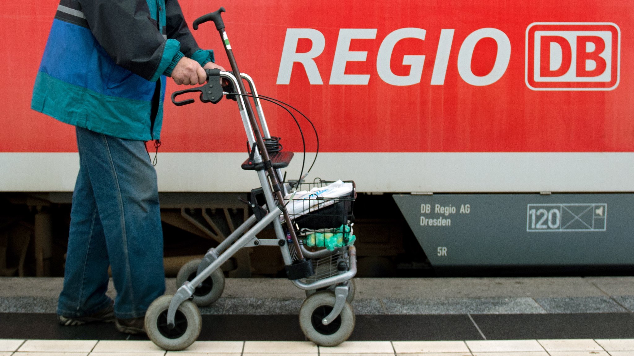 Ein Mann läuft mit seinem Rollator an einem Regionalzug der Deutschen Bahn vorbei.