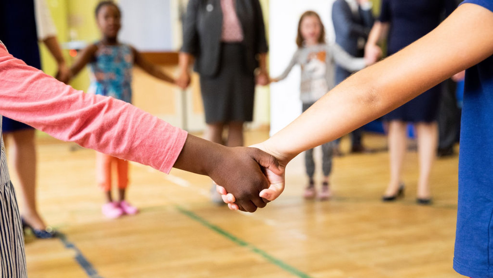 ARCHIV - 07.08.2019, Hamburg: Hand in Hand tanzen Kinder und Erzieherinnen bei einem Bewegungsspiel in der Turnhalle einer Kita. Die Situation in Kitas ist am 9. Februar Thema einer Aktuellen Stunde im Bundestag. Foto: Christian Charisius/dpa +++ dpa-Bildfunk +++