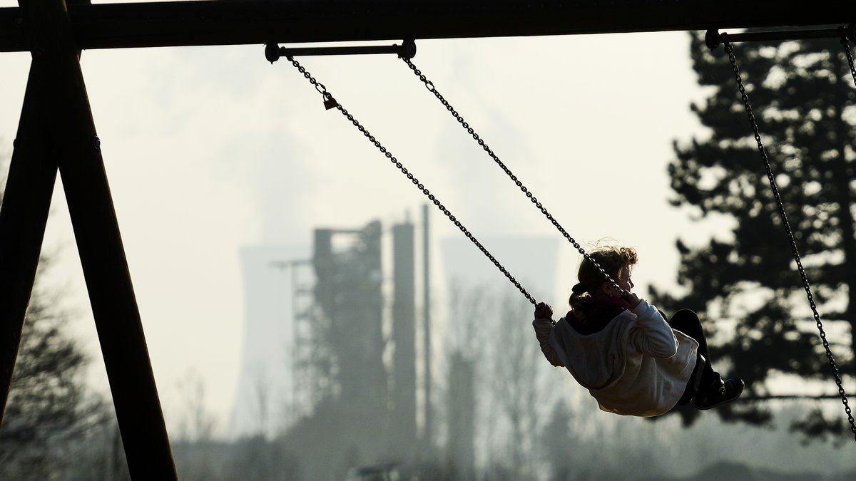 Kind auf Schaukel vor dem Hintergrund eines Atomkraftwerks
