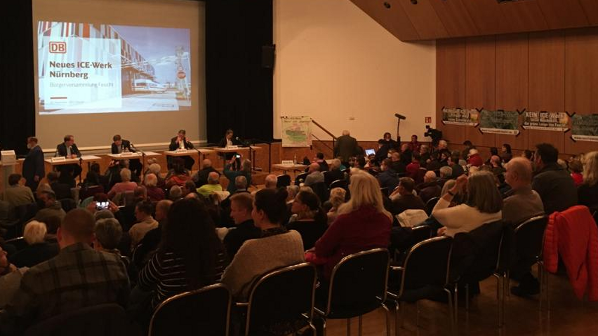 Ein Saal mit Menschen, vorn an der Bühne steht auf einer Leinwand "Neues ICE-Werk Nürnberg"