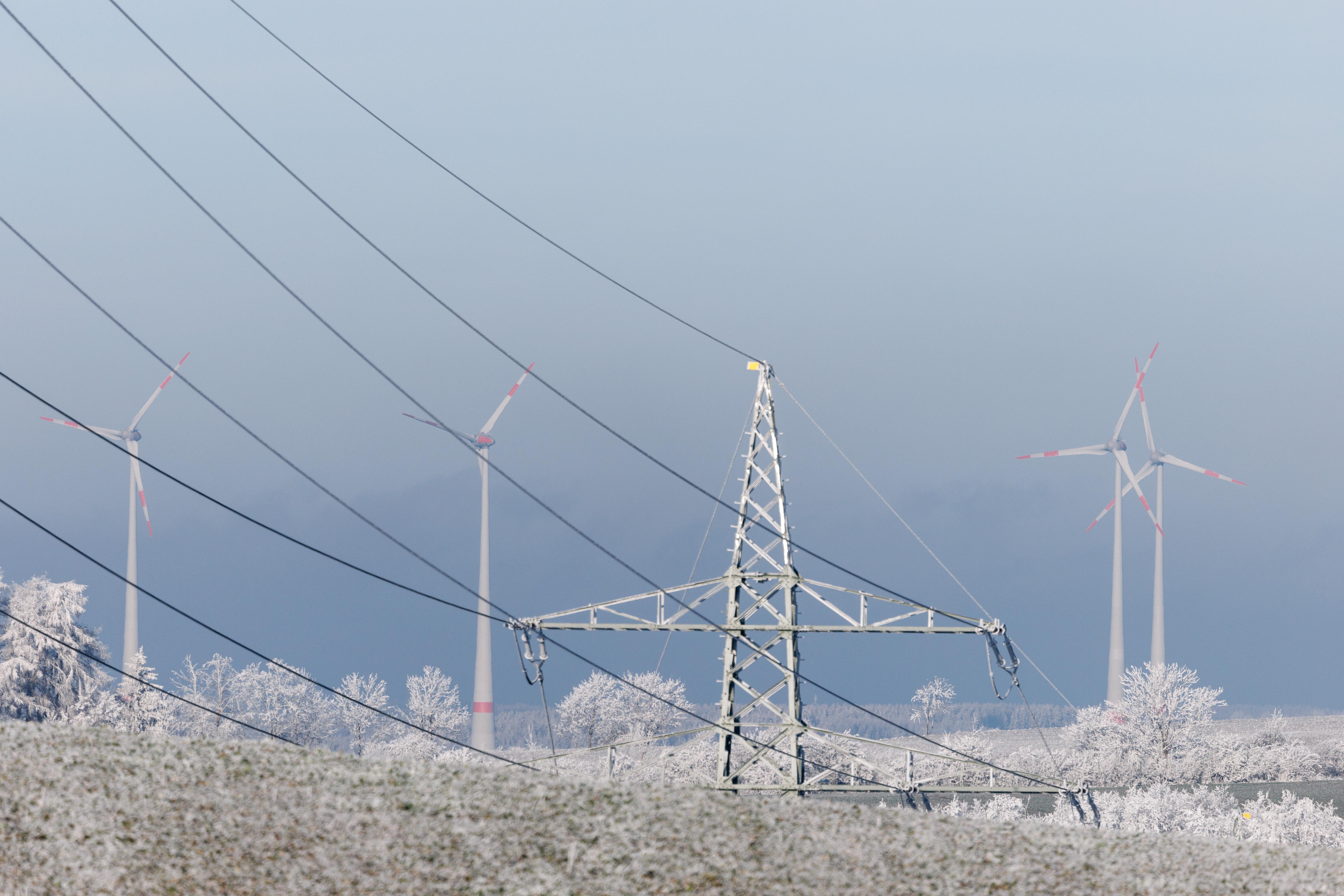 Windkraftanlagen sind am 31.12.2024 hinter einer Hochspannungsleitung nahe der Stadt Hof zu sehen.