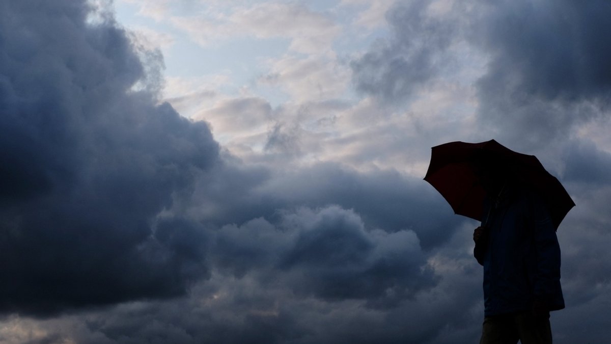 Eine Person steht mit Regenschirm vor großen Regenwolken.