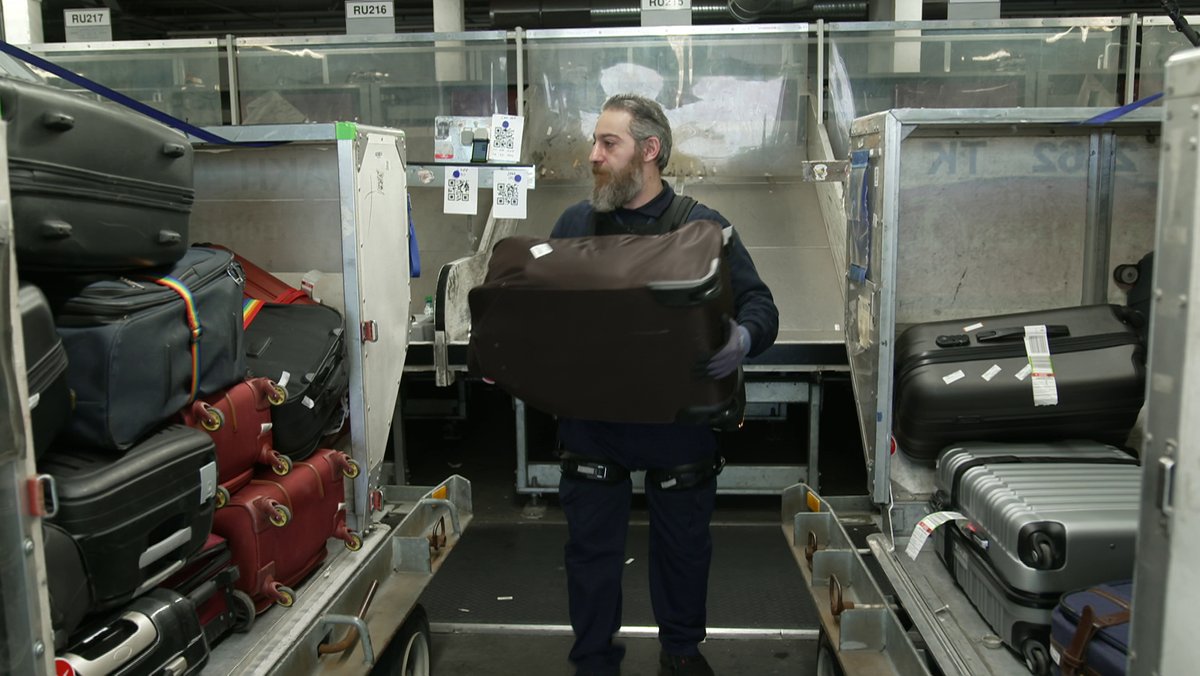 Mann verlädt Koffer in der Gepäckabfertigung