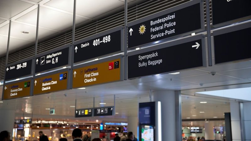 Schilder am Münchner Flughafen weisen auf Check-In-Schalter und Polizeidiensstellen hin