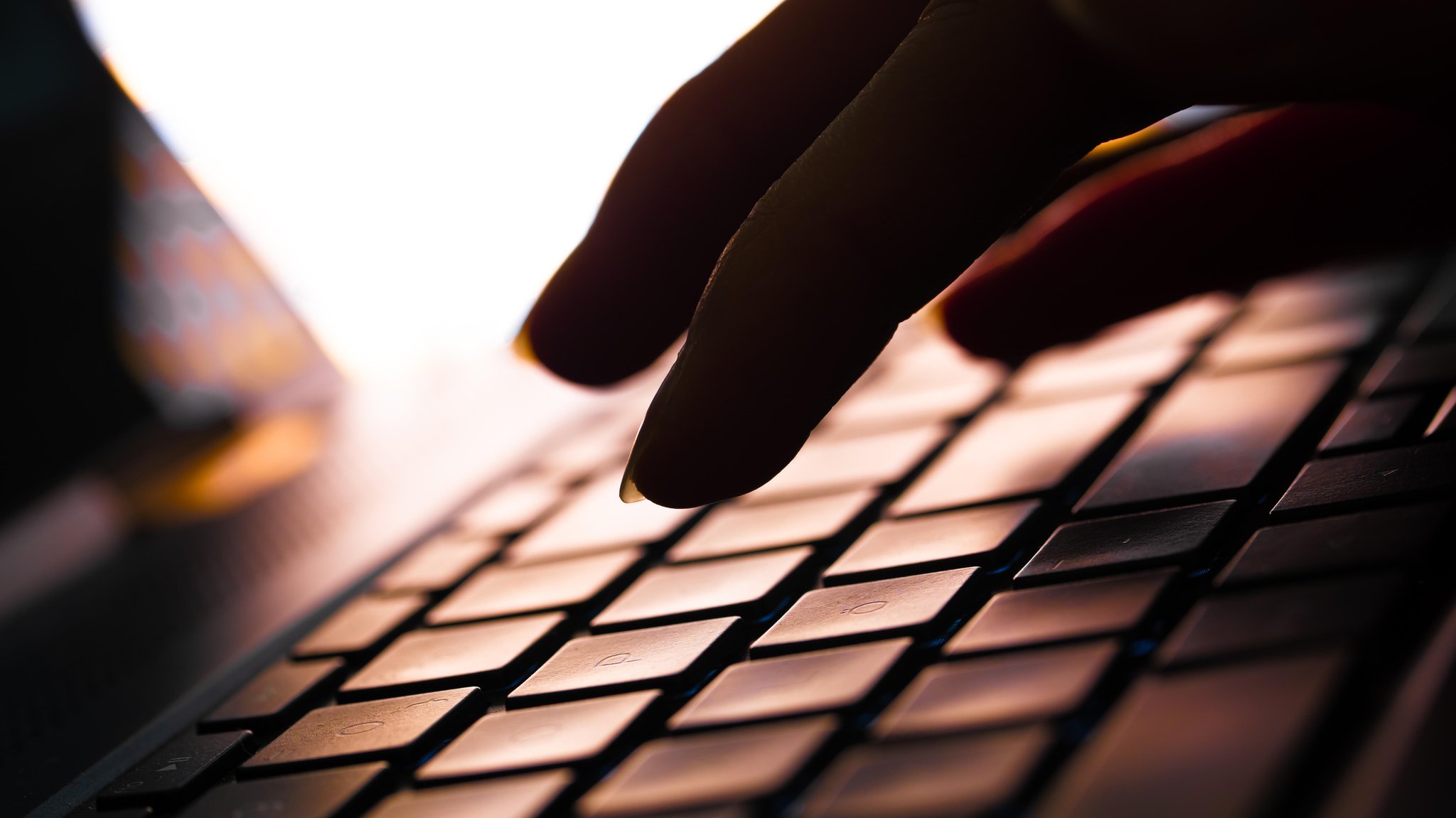 (Symbolbild) Unscharfes Bild mit Fingern, die auf einer dunklen Laptop-Tastatur tippen.