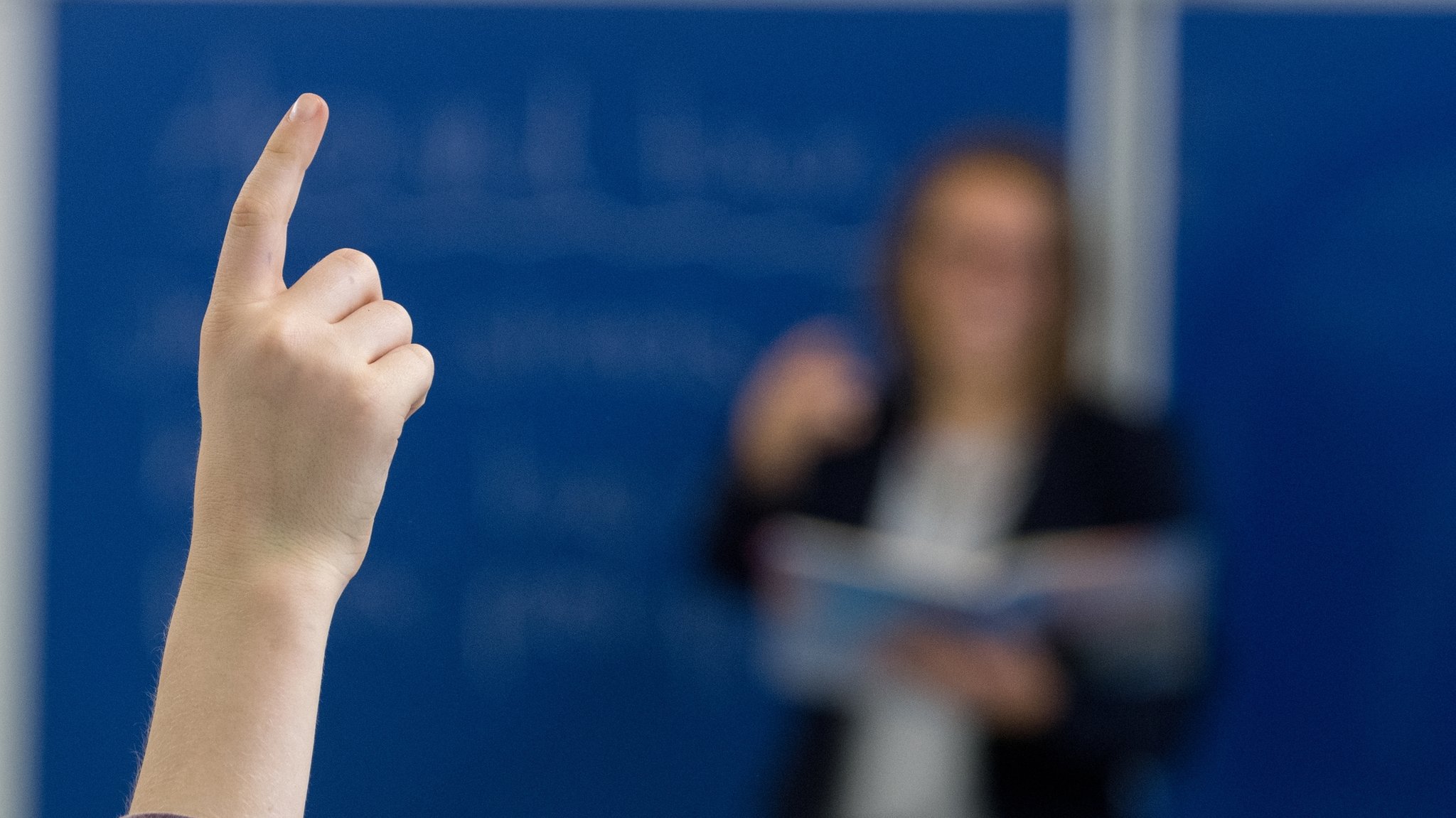 Ein Schüler meldet sich. Im Hintergrund steht eine Lehrerin. Von kurzfristigen Versetzungen sind vor allem angehende Lehrkräfte betroffen. 