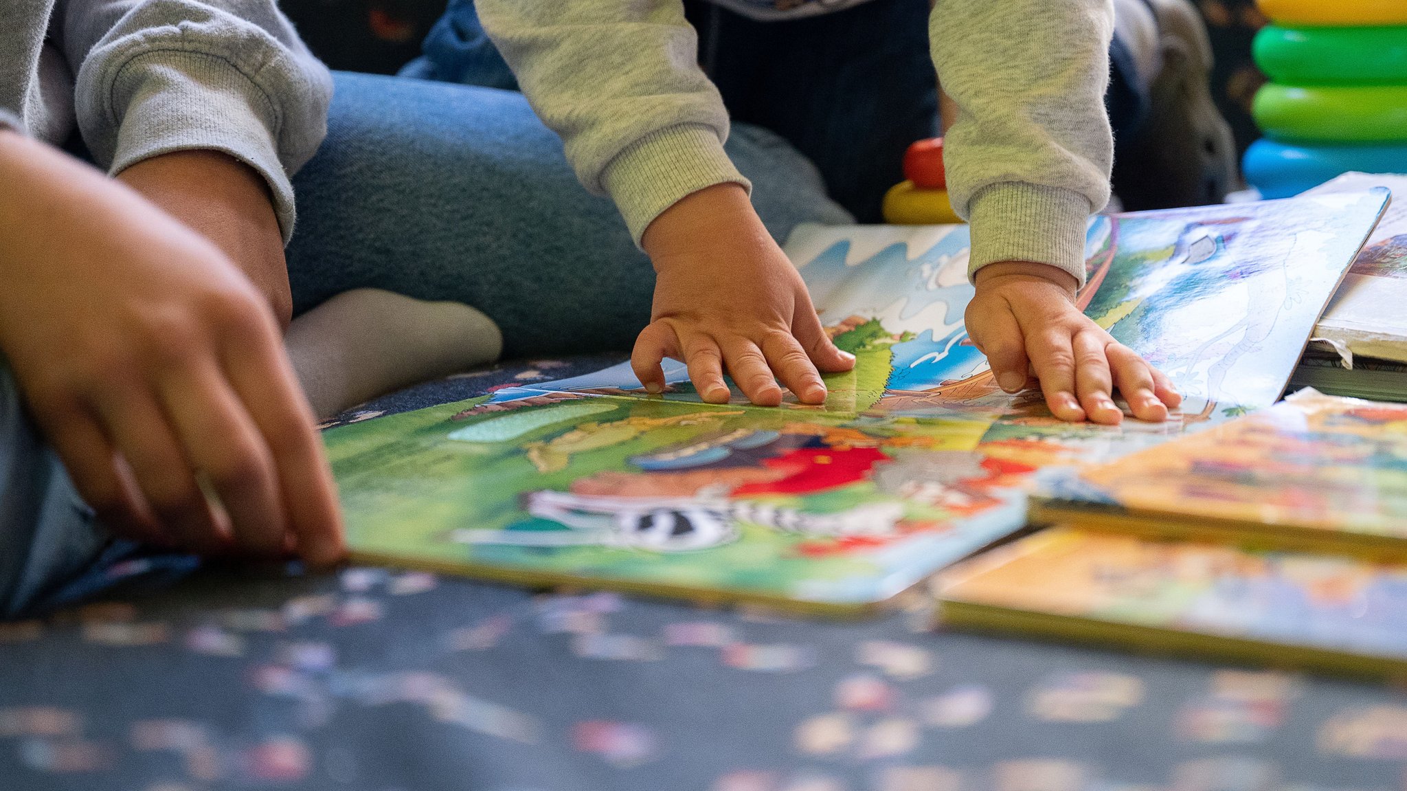 (Symbolbild) Kinder lesen ein Bilderbuch, man sieht ihre Hände auf dem Buch.