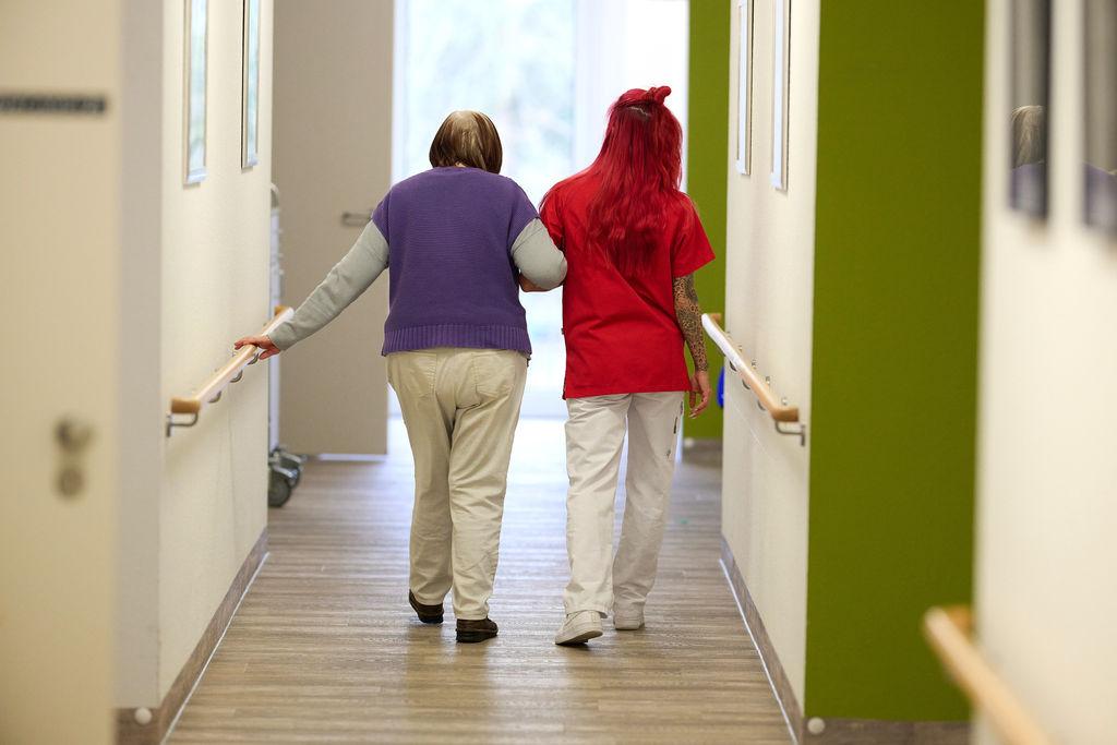 Eine Pflegekraft begleitet in einem Pflegezentrum eine Seniorin durch den Flur.