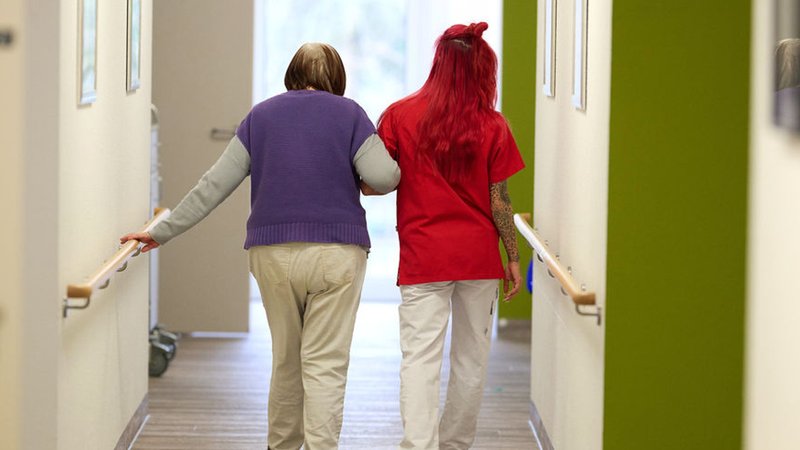 Eine Pflegekraft begleitet in einem Pflegezentrum eine Seniorin durch den Flur. | Bild: dpa-Bildfunk/Bernd Thissen Eine Pflegekraft begleitet in einem Pflegezentrum eine Seniorin durch den Flur.