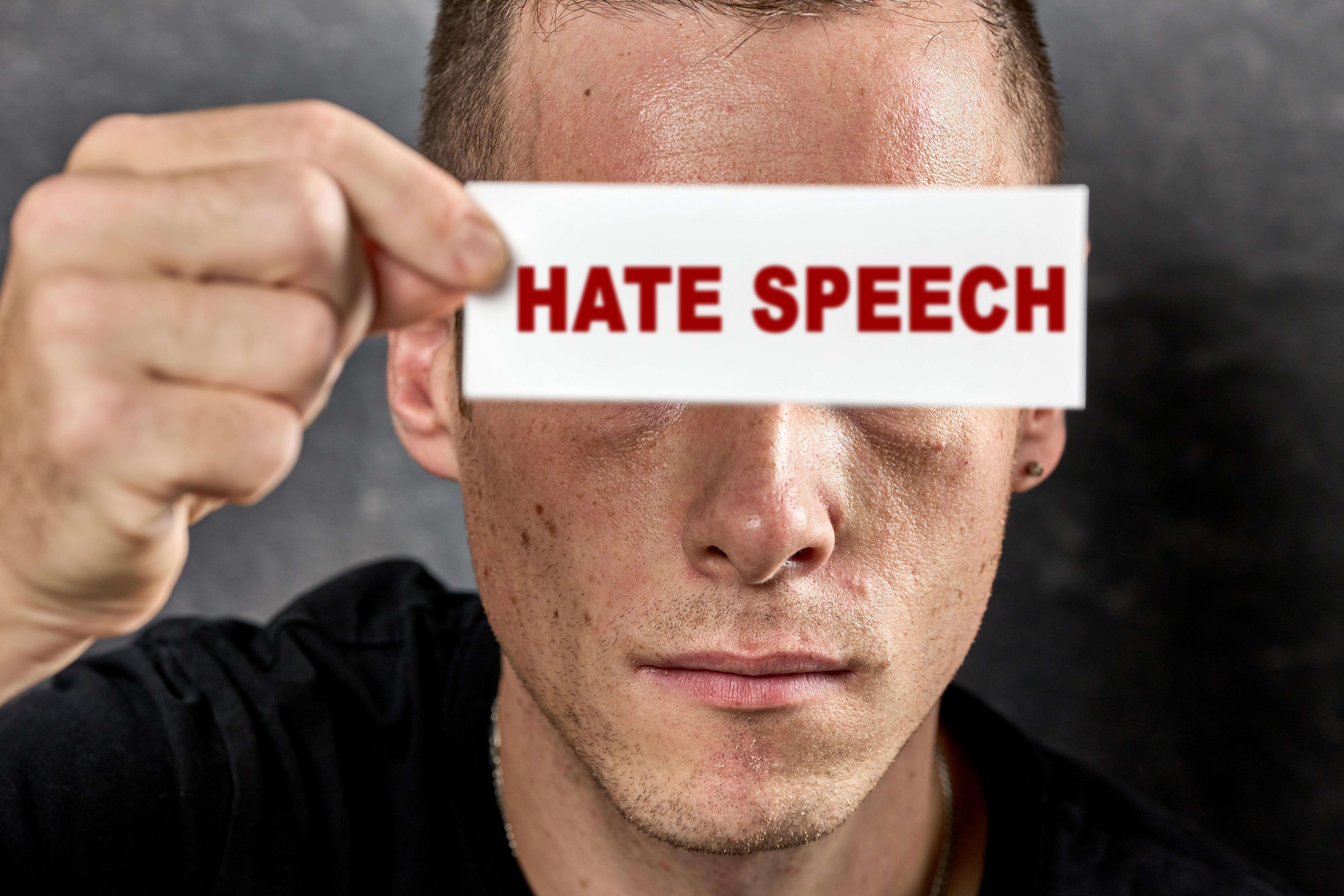 (Symbolbild): Ein Mann hält ein Schild mit der Aufschrift: Hate Speech, vor seine Augen.