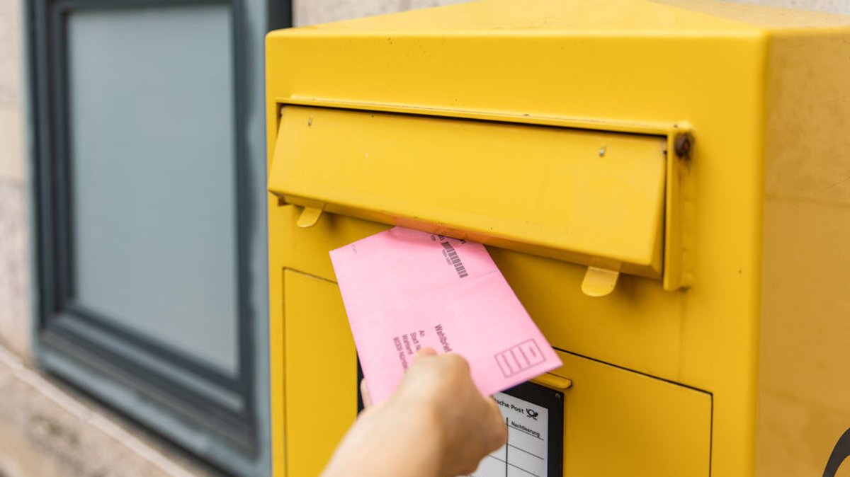 Eine Frau wirft ihre Briefwahlunterlagen in einen Briefkasten.