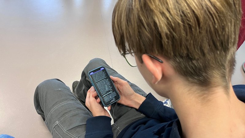 Junge schaut auf sein Smartphone, auf dem ein Text geöffnet ist