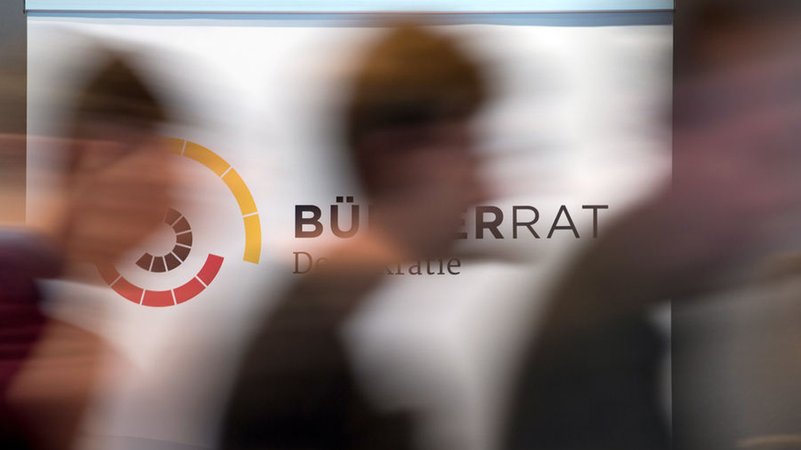 ARCHIV - 13.09.2019, Sachsen, Leipzig: Teilnehmer des Bürgerrates Demokratie in Leipzig gehen an einem Aufsteller mit dem Logo der Veranstaltung vorüber. (zu dpa: «Erster Bürgerrat in NRW soll 2026 Arbeit aufnehmen») Foto: Hendrik Schmidt/dpa-Zentralbild/dpa +++ dpa-Bildfunk +++ | Bild: dpa-Bildfunk/Hendrik Schmidt ARCHIV - 13.09.2019, Sachsen, Leipzig: Teilnehmer des Bürgerrates Demokratie in Leipzig gehen an einem Aufsteller mit dem Logo der Veranstaltung vorüber. (zu dpa: «Erster Bürgerrat in NRW soll 2026 Arbeit aufnehmen») Foto: Hendrik Schmidt/dpa-Zentralbild/dpa +++ dpa-Bildfunk +++