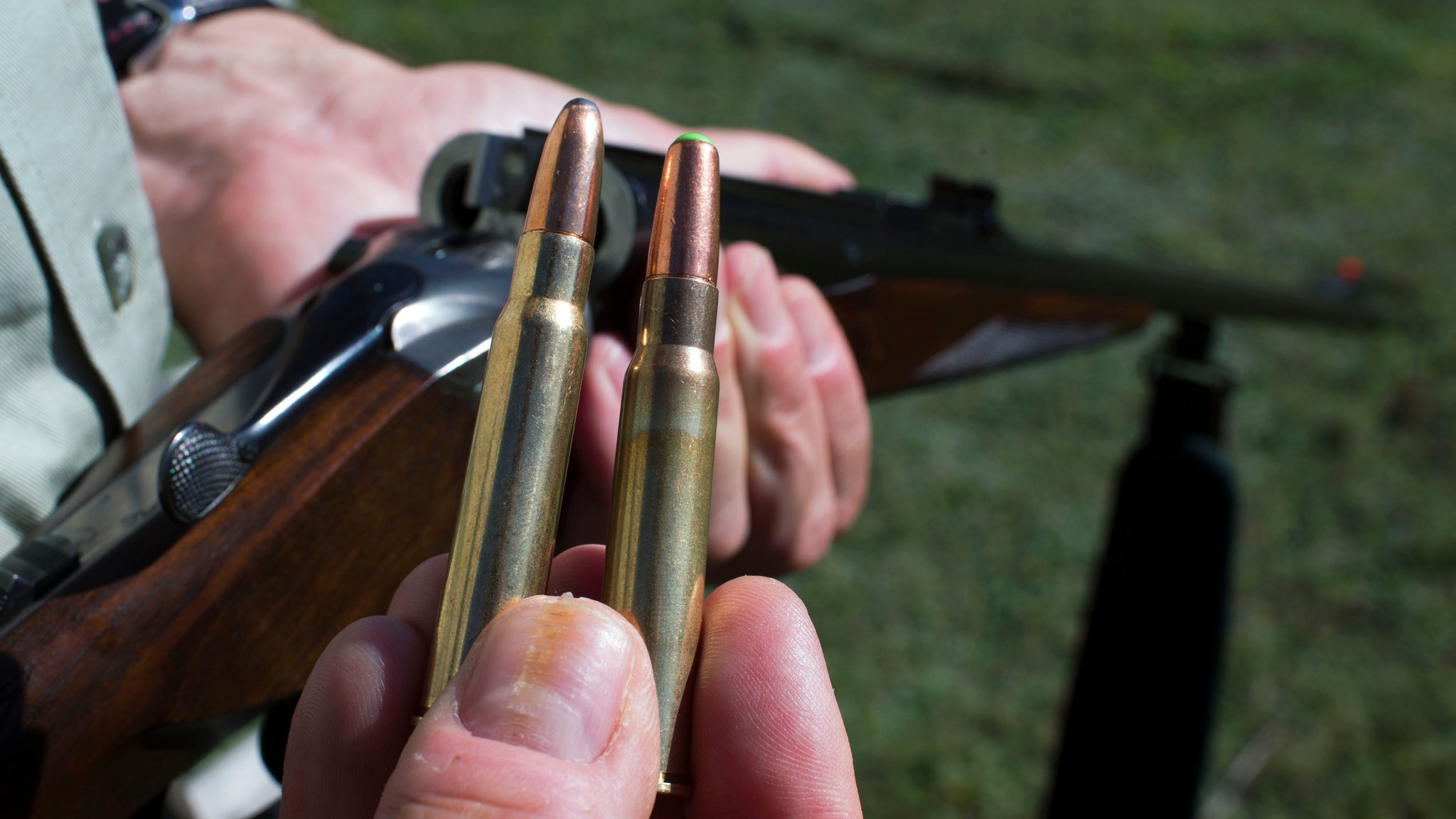 Ein Jäger hält in der einen Hand ein Jagdgewehr und in der anderen Munition mit und ohne Blei