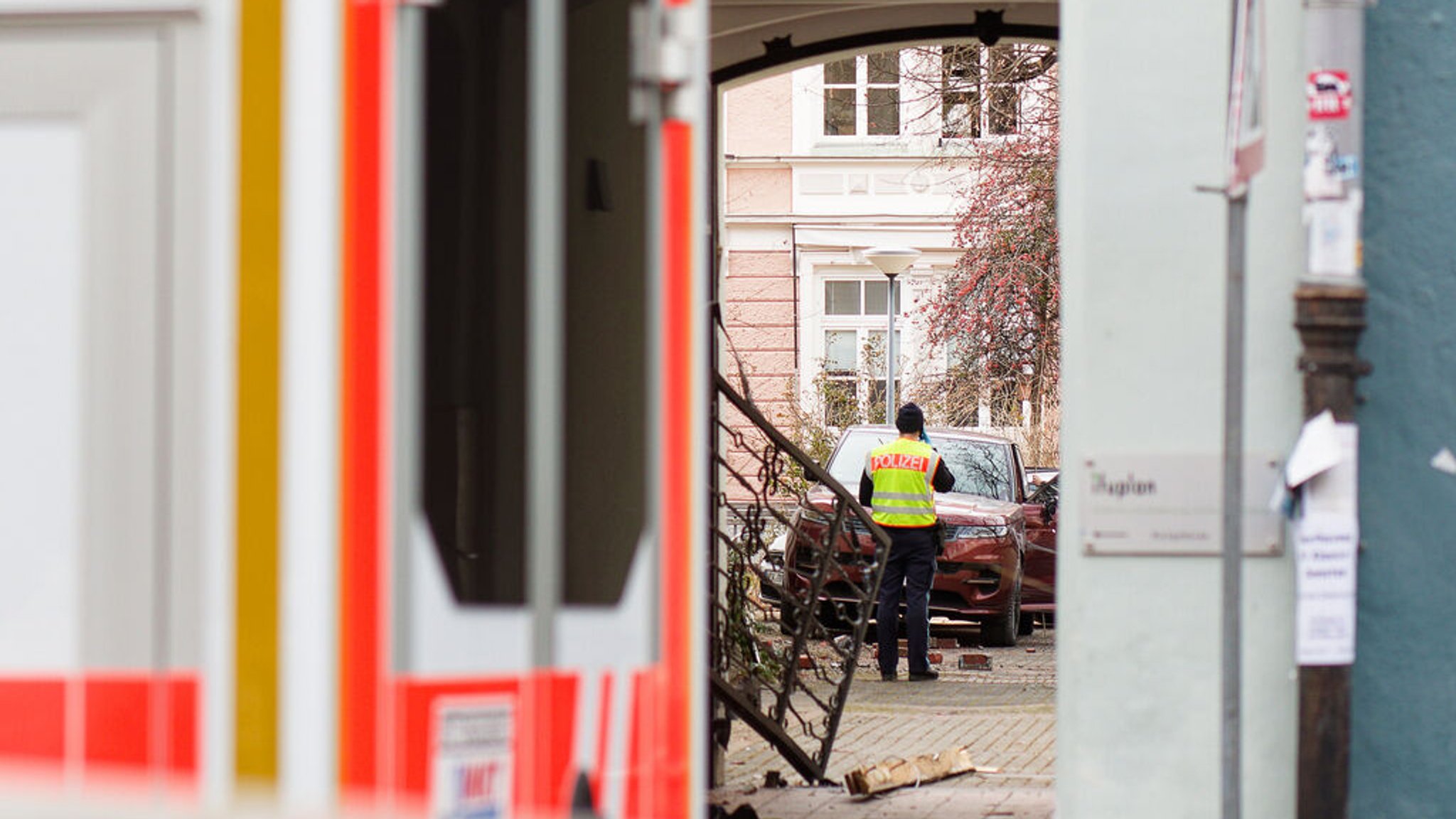 24.02.2025, Bayern, München: Ein Polizist steht in der Innenstadt neben einem beschädigten Hoftor. Eine Frau ist laut Polizei mit ihrem Auto durch ein Hoftor gebrochen und hat in der Einfahrt eine Fußgängerin überrollt. Die 22-Jährige sei noch am Unfallort reanimiert worden, sagte eine Polizeisprecherin. Foto: Tizian Gerbing/dpa +++ dpa-Bildfunk +++