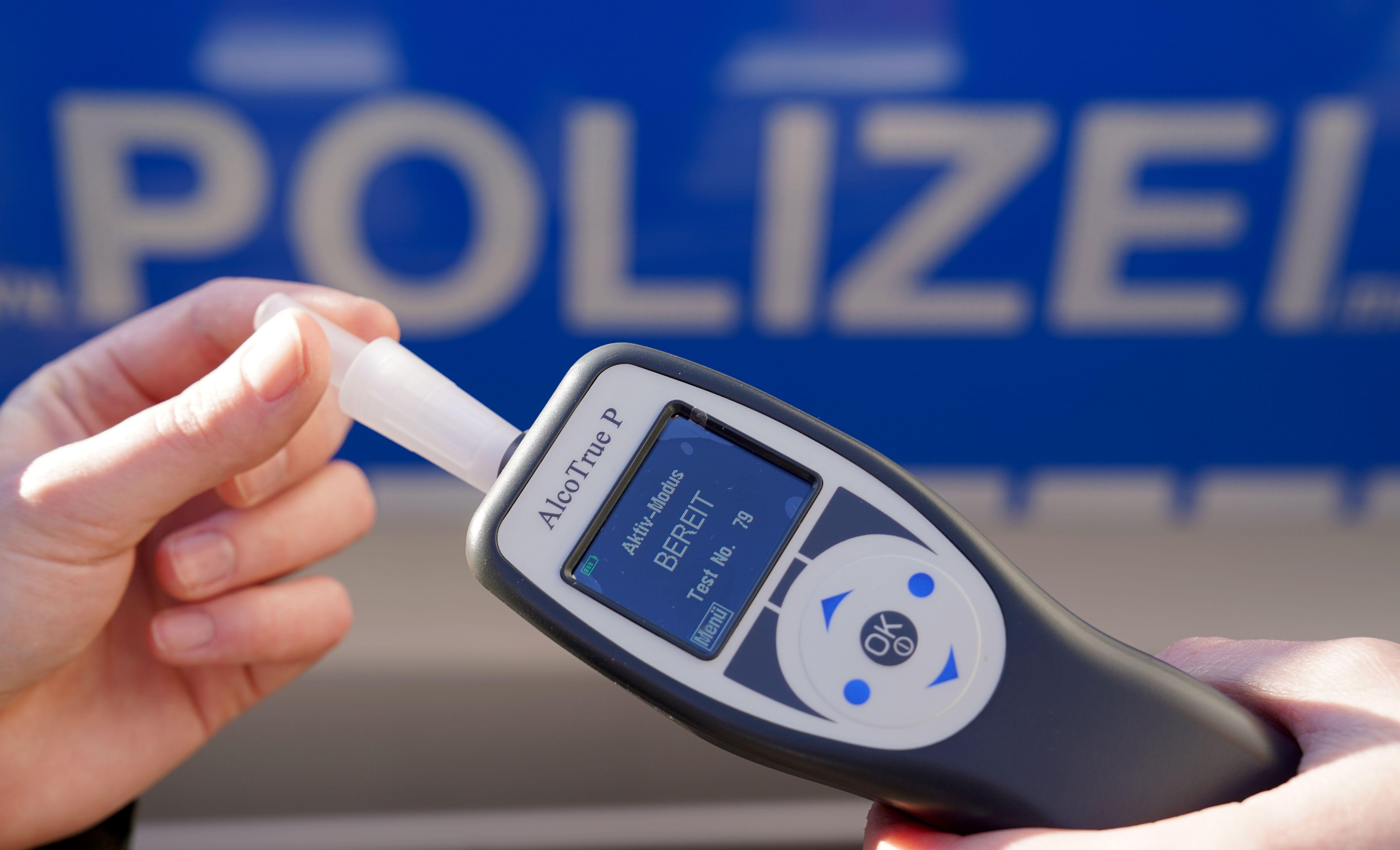 Ein Polizist hält ein Atemalkohol-Messgerät zur Überprüfung der Fahrtüchtigkeit eines Autofahrers in der Hand.