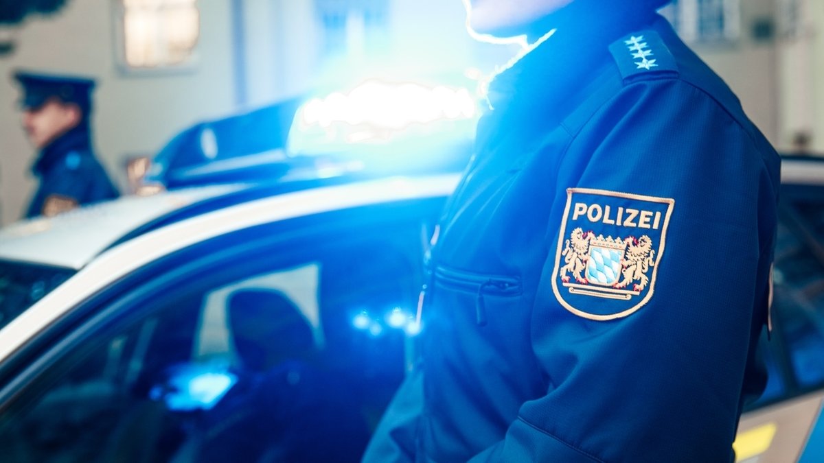 Eine Polizistin und ein Polizist stehen neben einem Polizeiauto mit Blaulicht (Symbolbild)