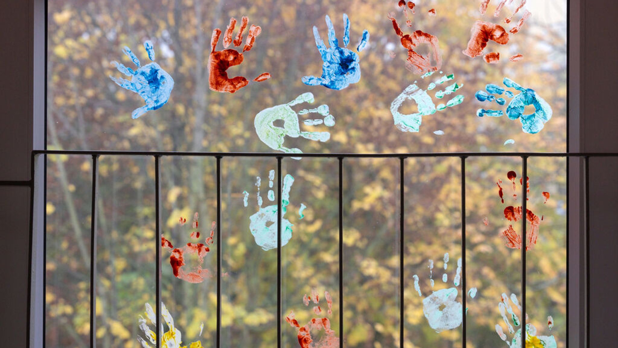 Kinder haben in einem Kindergarten farbige Abdrücke ihrer Hände auf einem Fenster hinterlassen. 