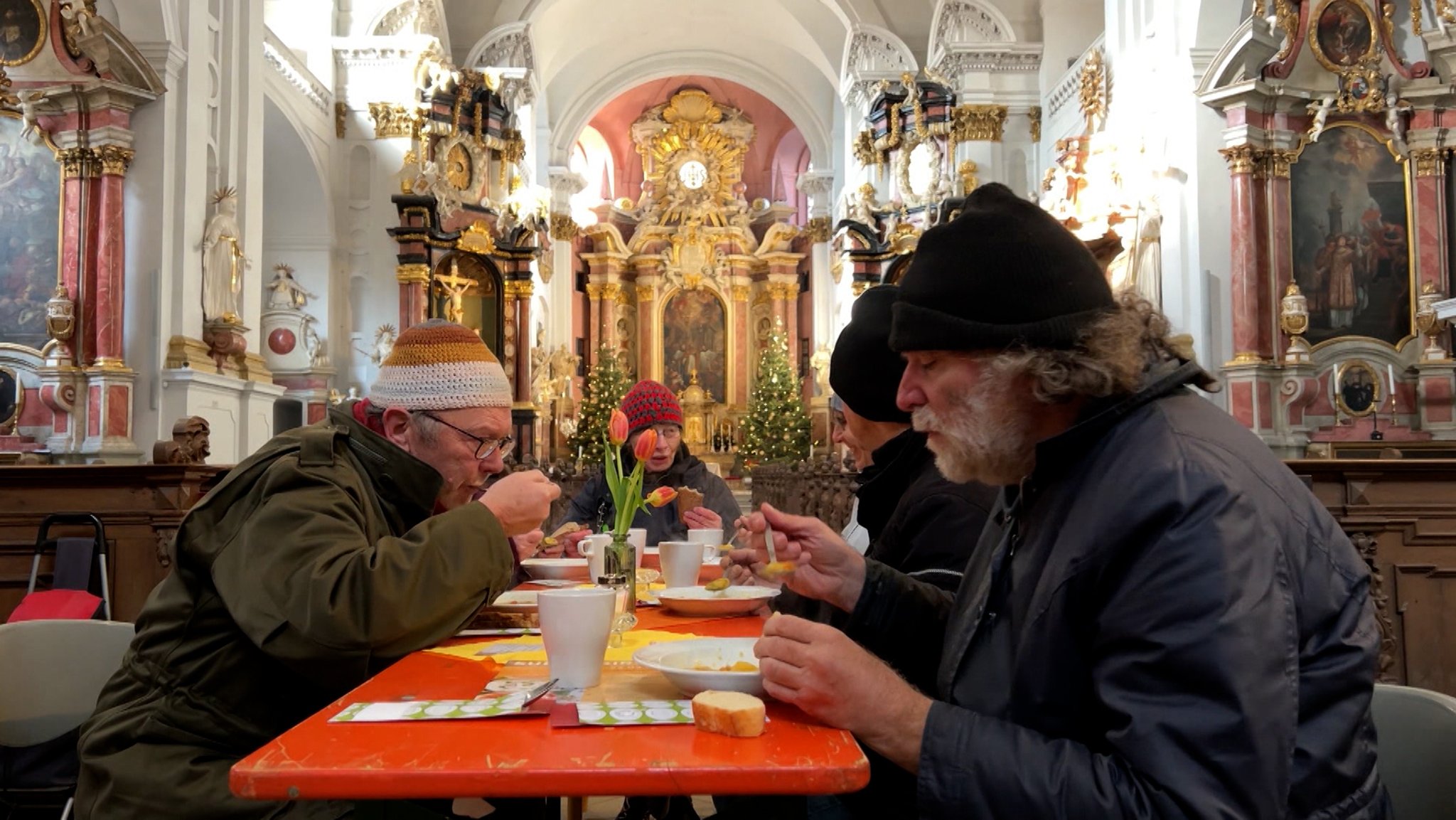 Menschen sitzen in einer Kirche am Tisch und essen Suppe.