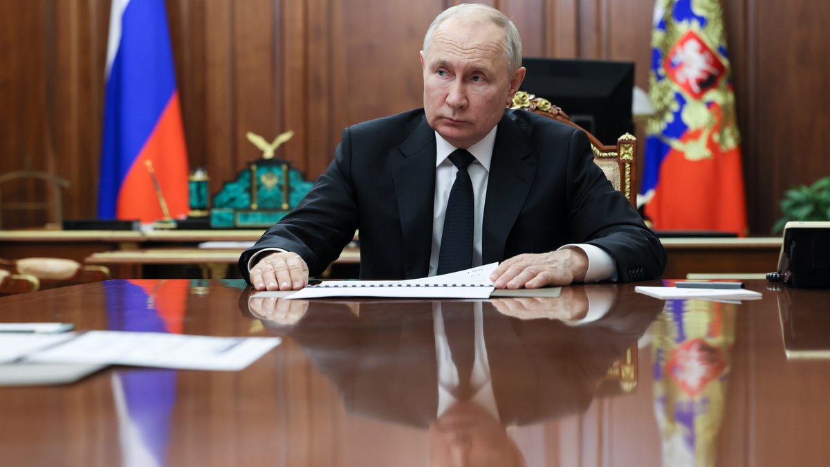 Der Präsident mit einer Unterlage vor russischen Fahnen 