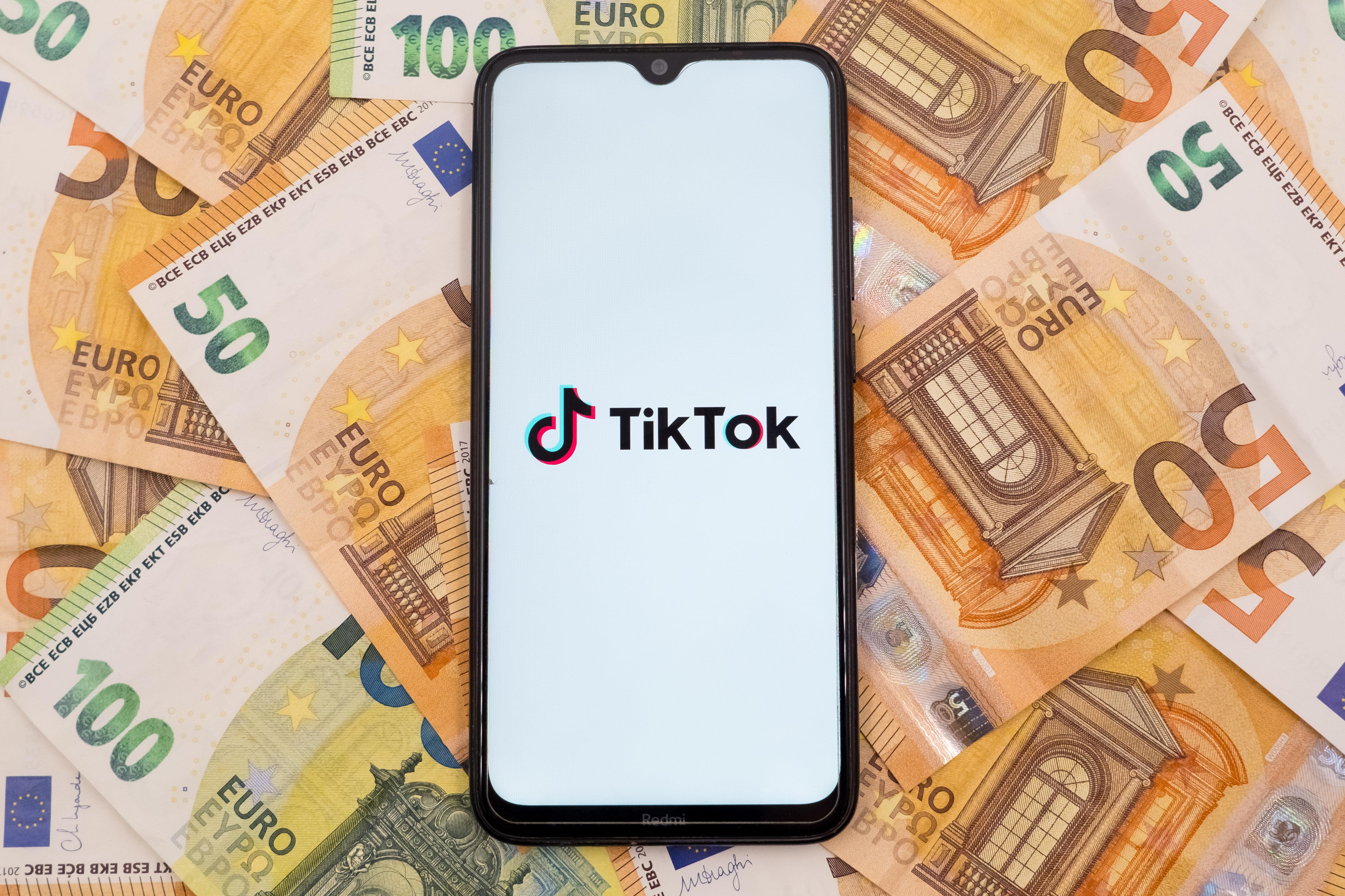 Ein Smartphone zeigt das TikTok-Logo, viele 50-Euro-Scheine im Hintergrund.