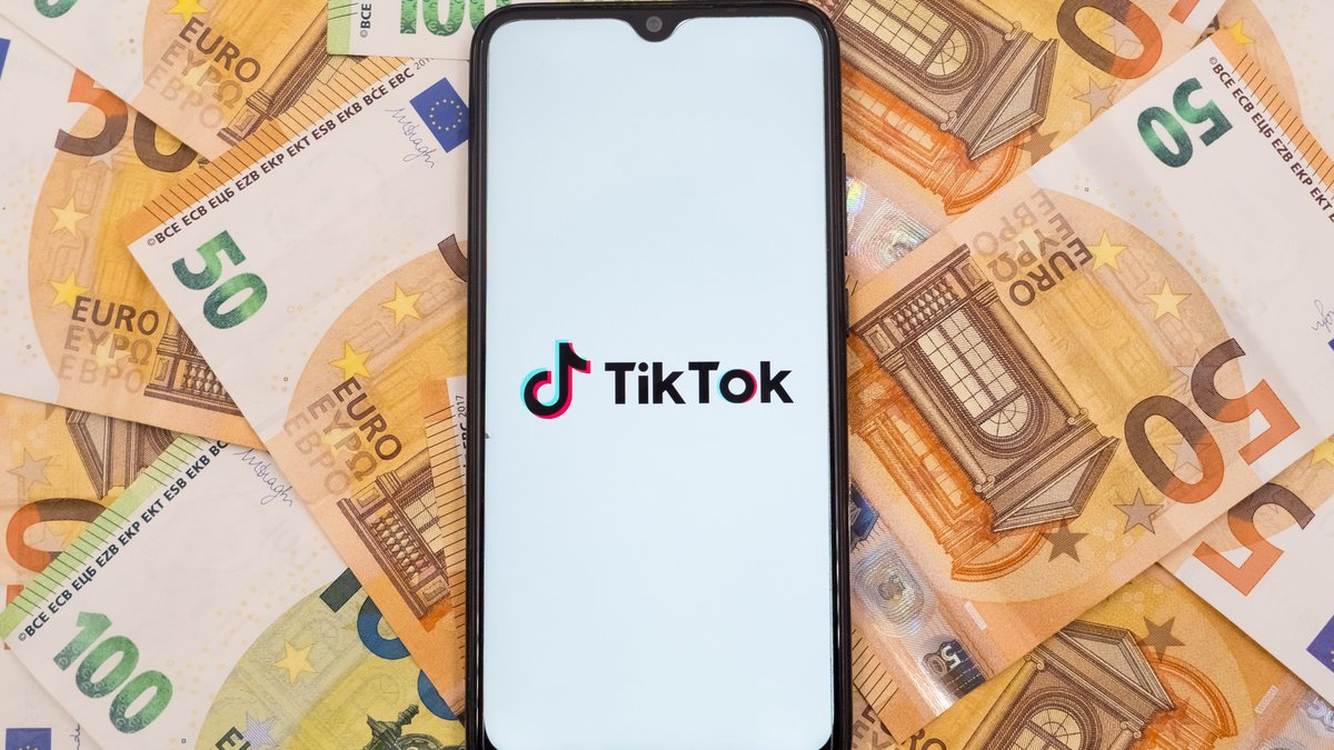 Ein Smartphone zeigt das TikTok-Logo, viele 50-Euro-Scheine im Hintergrund.