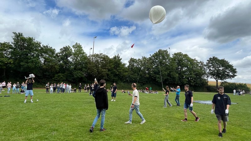 Schülerinnen und Schüler der Realschule Dettelbach stehen auf einer Wiese und lassen einen Wetterballon aufsteigen.