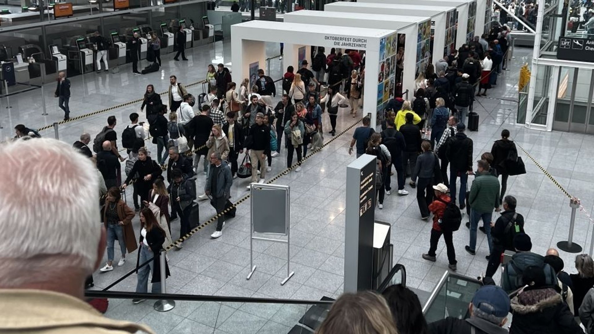 Blick von einer Treppe auf ein Foyer am Münchner Flughafen, durch das sich eine lange Menschenschlange zieht. Für das Chaos am gestrigen Donnerstag musste sich der Flughafen heute erklären.