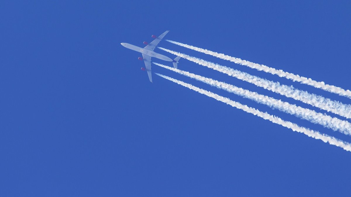 Kondensstreifen aus Triebwerksabgasen, cirrus aviaticus, die sich hinter einem viermotorigen Flugzeug vom Typ Airbus A340 am blauen Himmel bilden; Umweltverträglich? Bericht zeigt Wege für "grünes" Fliegen