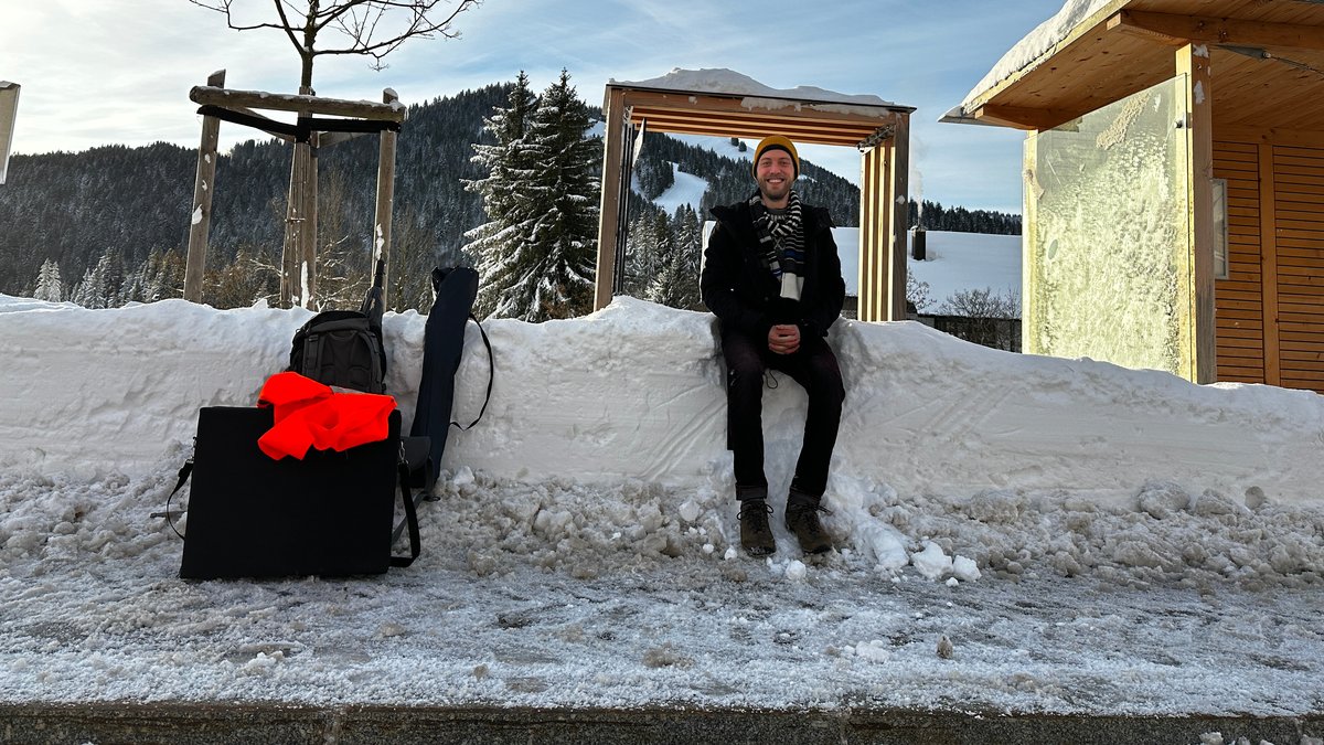 Der Reporter sitzt auf dem Schneeblock auf der Mitfahrbank in Balderschwang und wartet auf eine Mitfahrgelegenheit nach Immenstadt