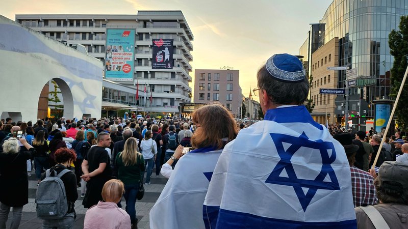 Ein Mann steht mit Kippa und Israel-Flagge um die Schultern vor vielen Menschen.