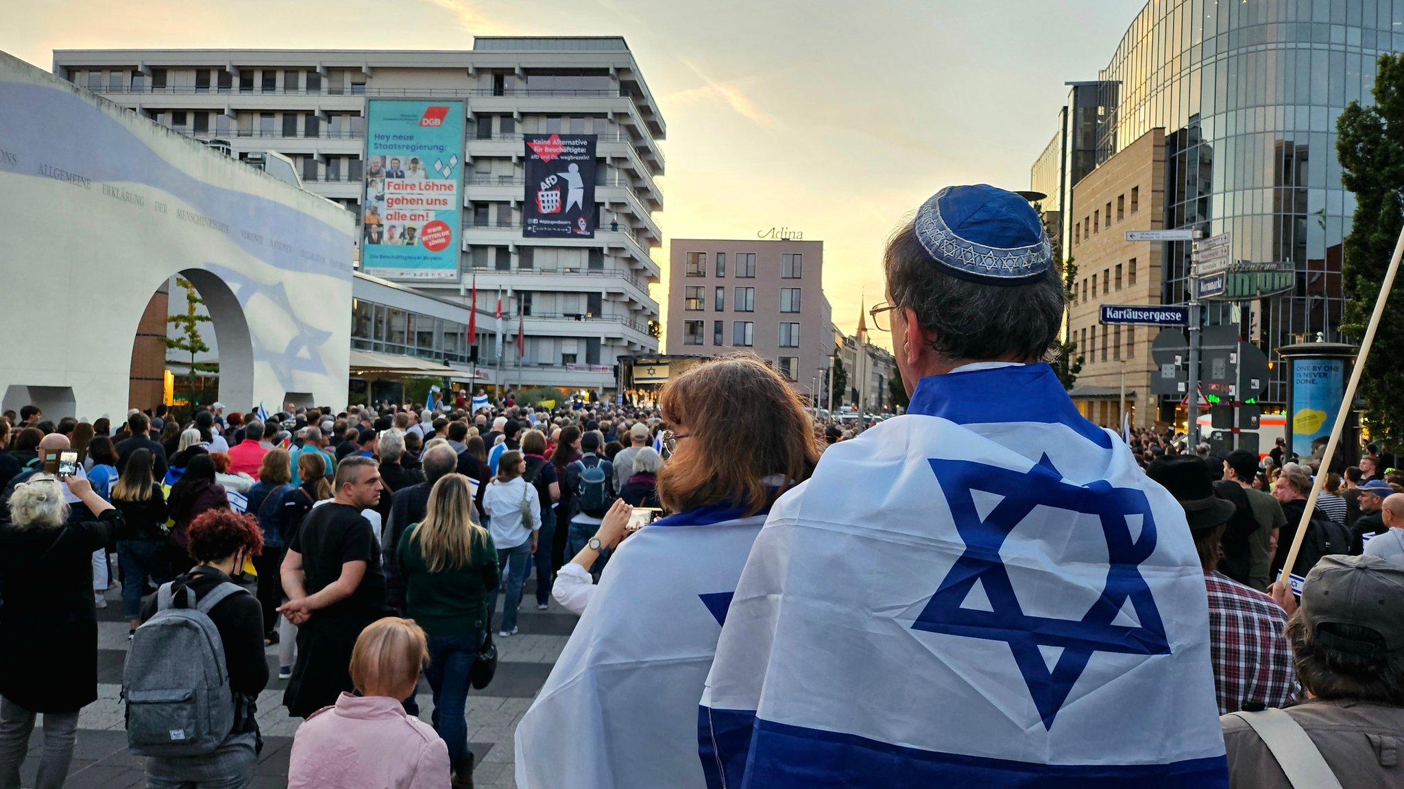 Ein Mann steht mit Kippa und Israel-Flagge um die Schultern vor vielen Menschen.