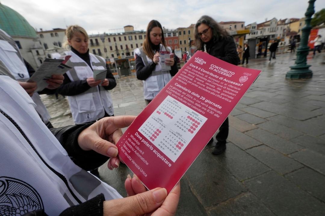 Kontrolleure überprüfen den QR-Code der Touristen vor dem Bahnhof in Venedig, während ein Kontrolleur einen Kalender der über die Eintrittsgebühr informiert. 