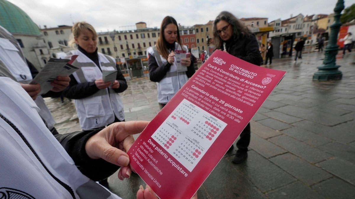Kontrolleure überprüfen den QR-Code der Touristen vor dem Bahnhof in Venedig, während ein Kontrolleur einen Kalender der über die Eintrittsgebühr informiert. 