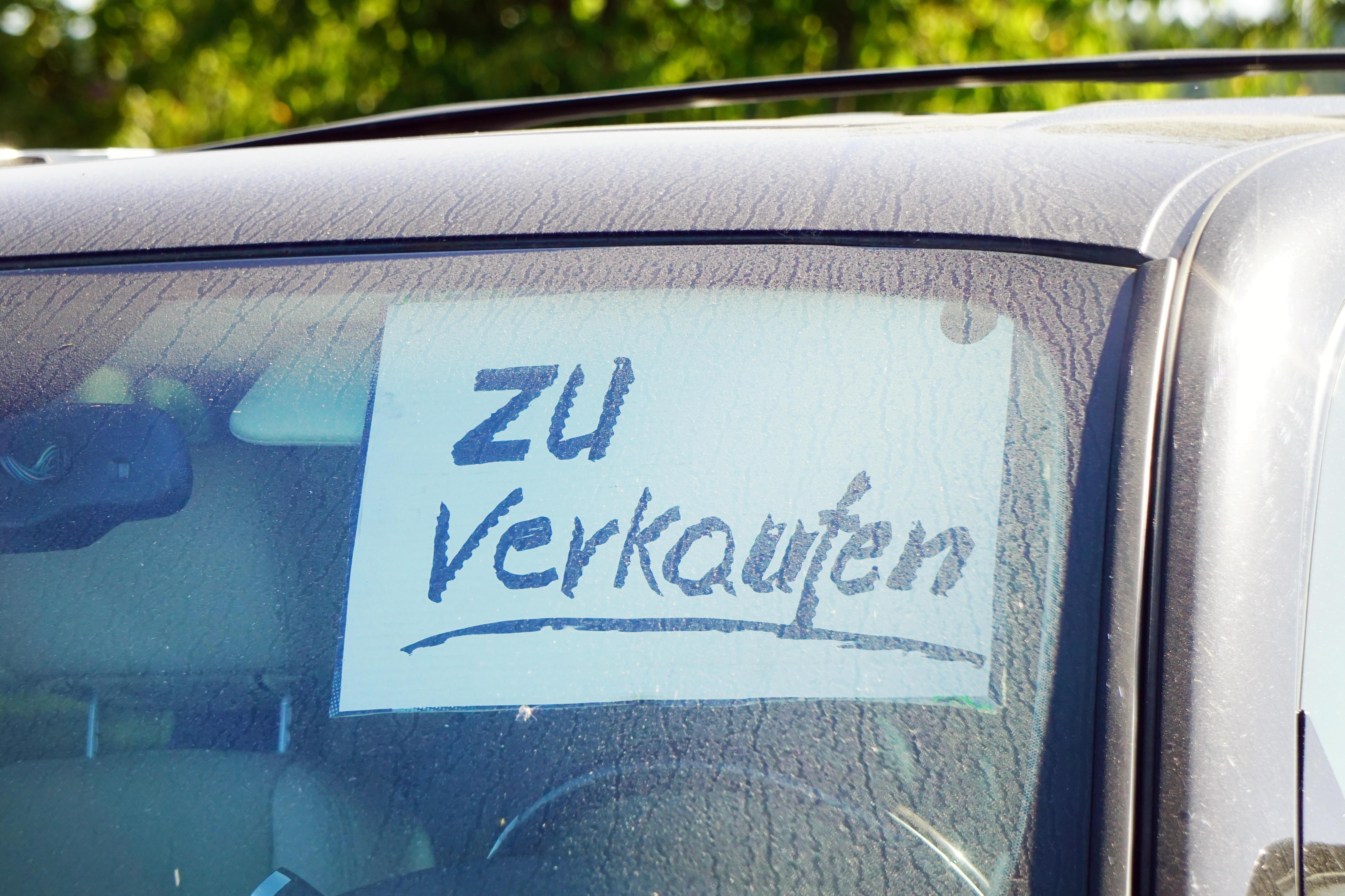In der Windschutzscheibe eines Autos klebt ein Schild: "Zu verkaufen".