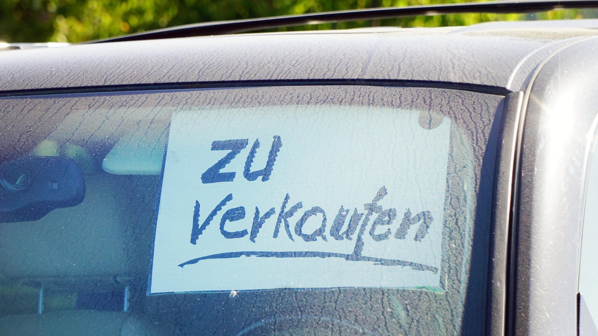 In der Windschutzscheibe eines Autos klebt ein Schild: "Zu verkaufen".