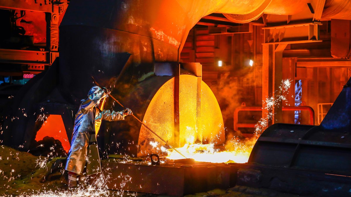 Ein Stahlarbeiter bei ThyssenKrupp entnimmt im Schutzanzug eine 1.500 Grad heiße Roheisenprobe am Hochofen. 
