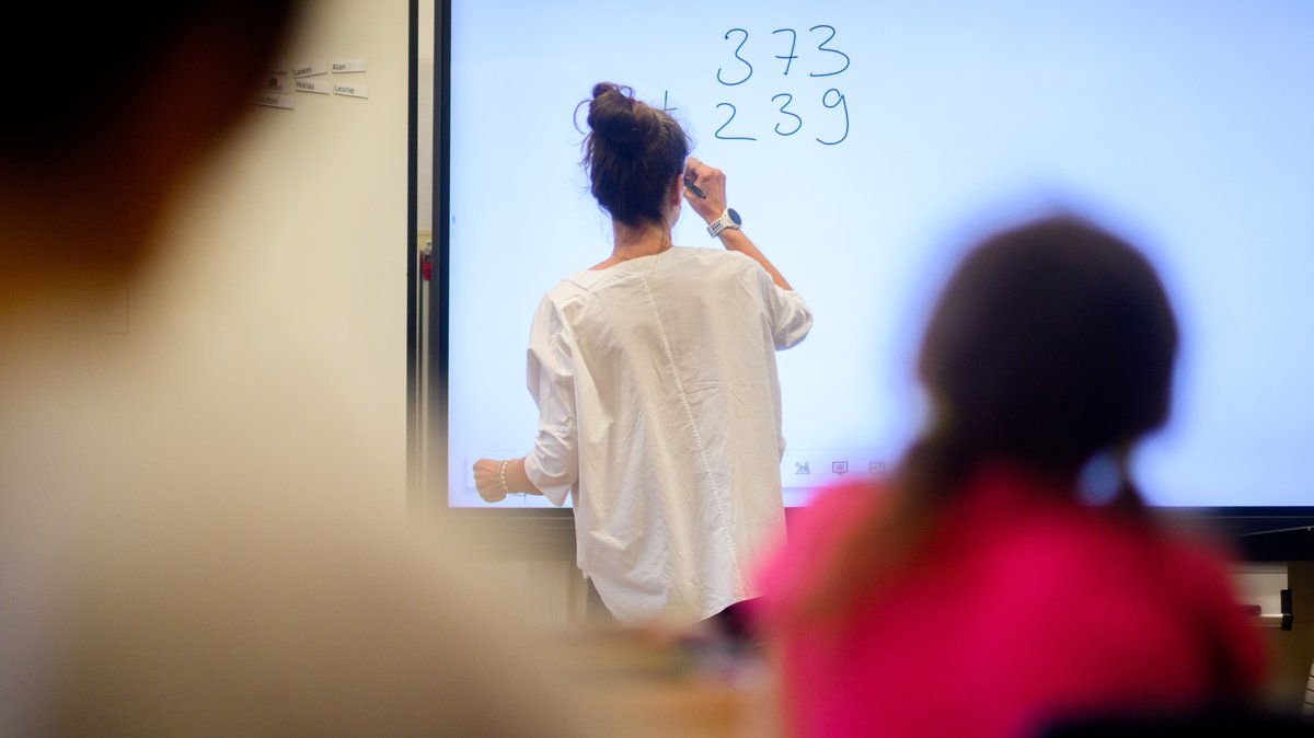 Eine Lehrerin schreibt eine Mathematikaufgabe auf eine digitale Schultafel im Klassenraum einer 4. Klasse (Symbolbild)